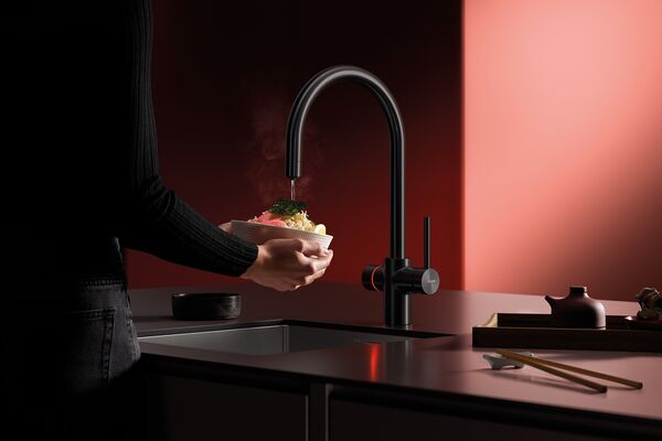 Utilisation d’un robinet multifonctions Laufen Vara pour verser de l’eau chaude sur un plat dans une cuisine moderne.